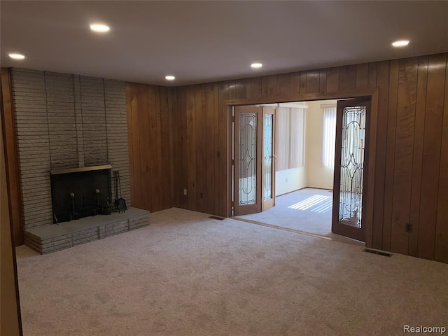 unfurnished living room with wood walls, carpet, a fireplace, and visible vents