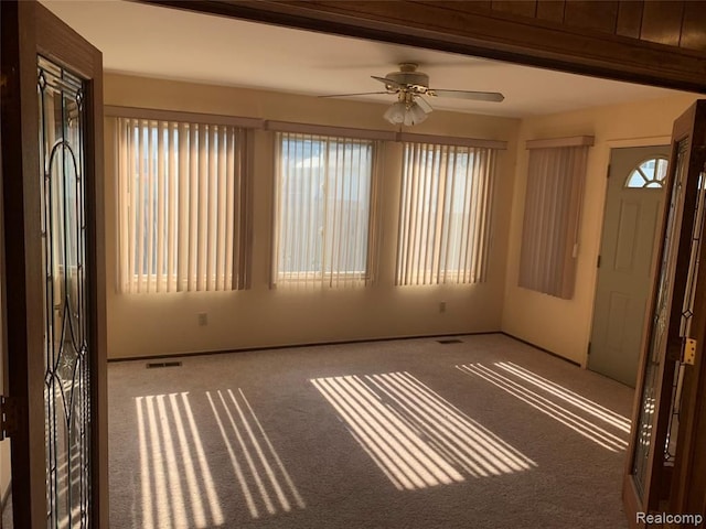 carpeted spare room with ceiling fan, visible vents, and a healthy amount of sunlight