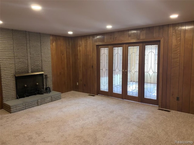 unfurnished living room with wood walls, carpet, visible vents, and a brick fireplace