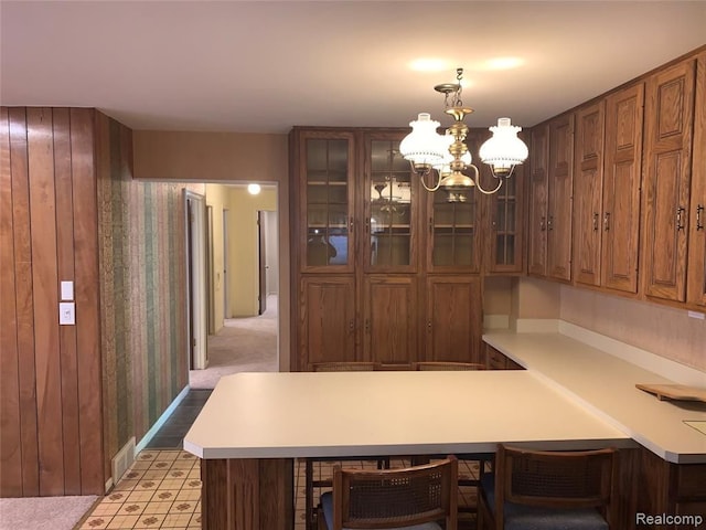 kitchen featuring a chandelier, a peninsula, a breakfast bar, light countertops, and glass insert cabinets