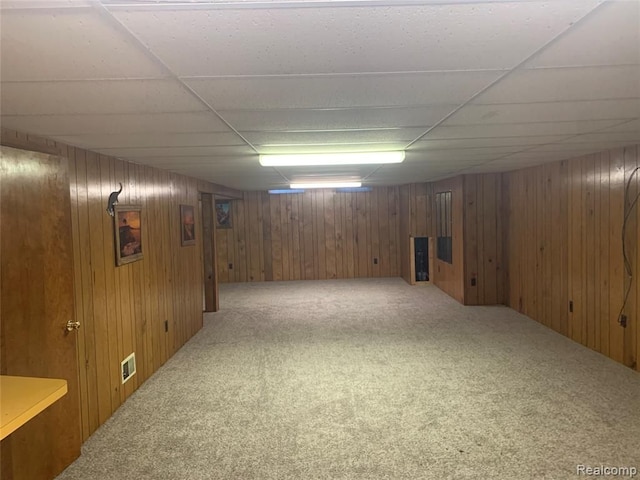 finished basement featuring carpet, wood walls, and a paneled ceiling