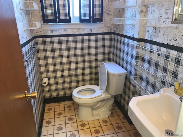 half bath featuring wainscoting, tile walls, toilet, and wallpapered walls