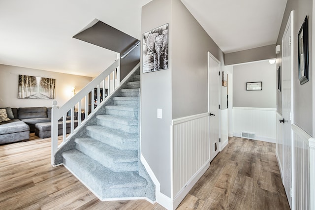 stairway with wainscoting, visible vents, and wood finished floors