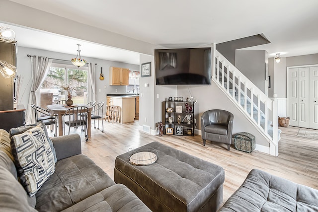 living area with light wood-style flooring, visible vents, stairway, and baseboards