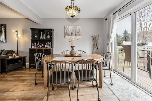 dining room with a dry bar, plenty of natural light, light wood-style flooring, and beamed ceiling