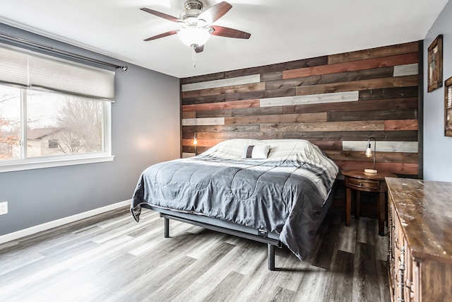 bedroom featuring an accent wall, a ceiling fan, wood walls, wood finished floors, and baseboards