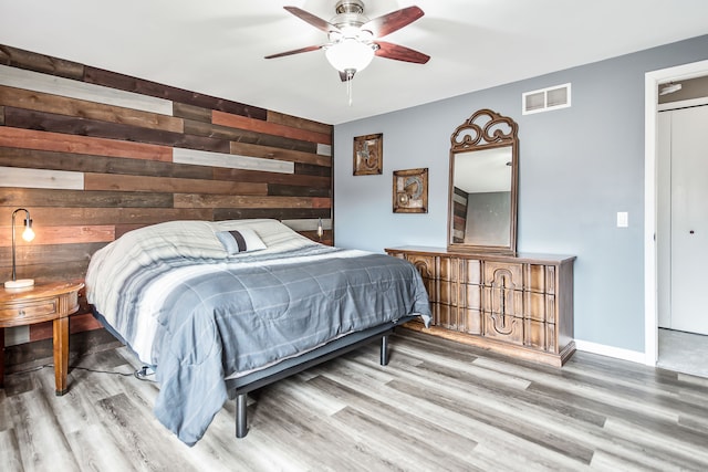 bedroom with an accent wall, wood walls, wood finished floors, and visible vents