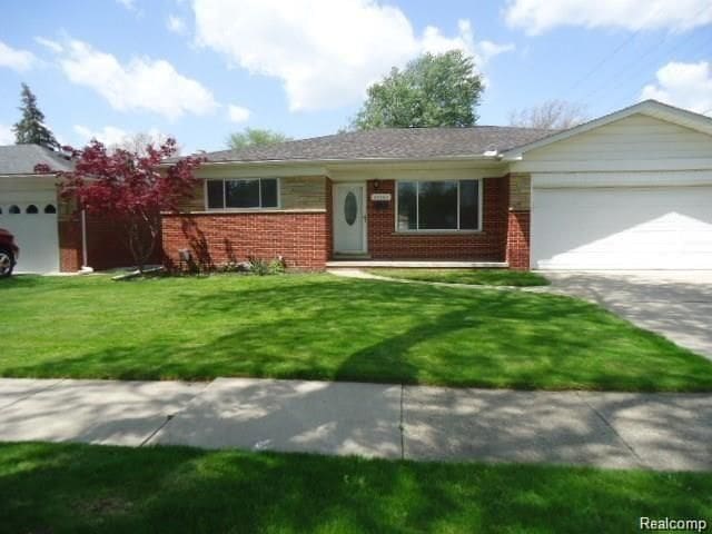 single story home with driveway, brick siding, an attached garage, and a front yard