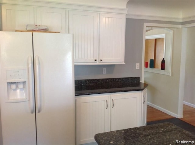 kitchen with baseboards, dark stone countertops, wood finished floors, white fridge with ice dispenser, and white cabinetry