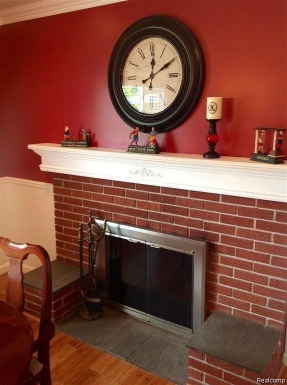 details featuring a brick fireplace, crown molding, and wood finished floors