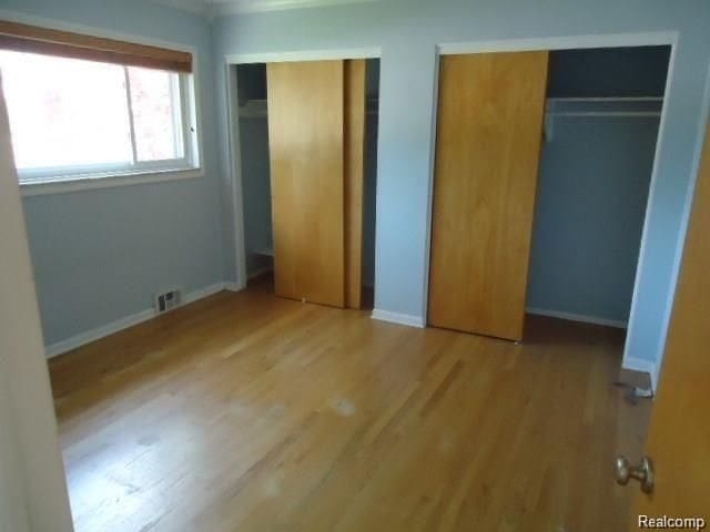 unfurnished bedroom featuring multiple closets, visible vents, baseboards, and wood finished floors