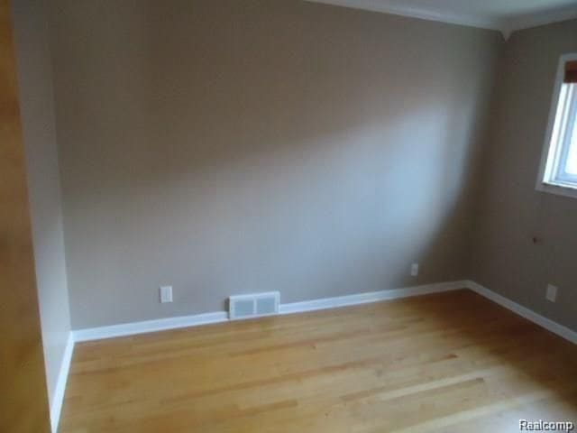 empty room with baseboards, visible vents, and wood finished floors