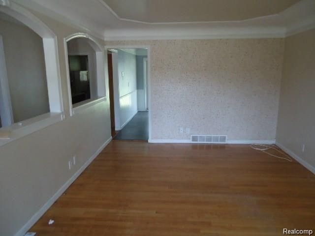 empty room featuring baseboards, visible vents, wood finished floors, and ornamental molding