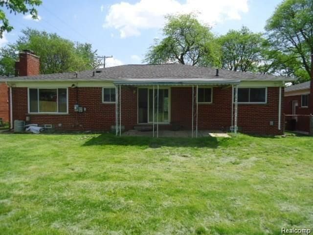 rear view of house with a yard, brick siding, and a chimney