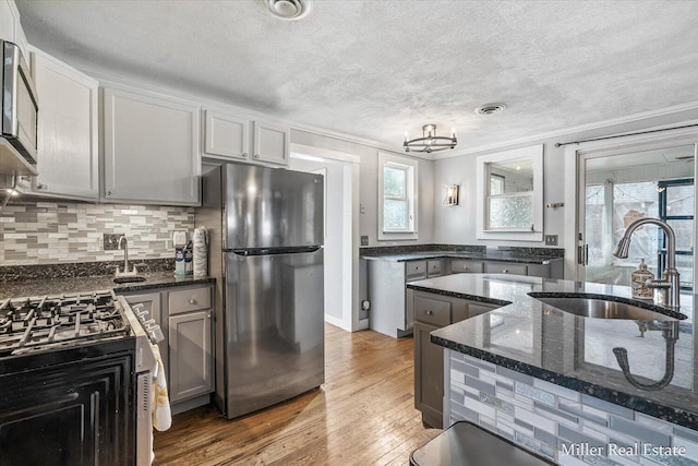 kitchen with stainless steel appliances, wood finished floors, a sink, visible vents, and dark stone counters