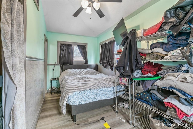 bedroom with a wainscoted wall, ceiling fan, vaulted ceiling, and wood finished floors