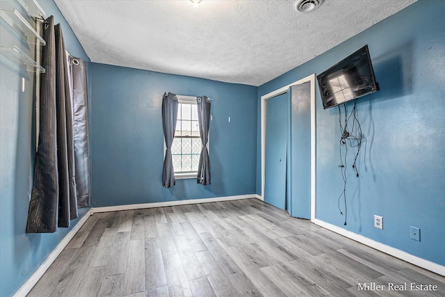 unfurnished bedroom with visible vents, a textured ceiling, baseboards, and wood finished floors