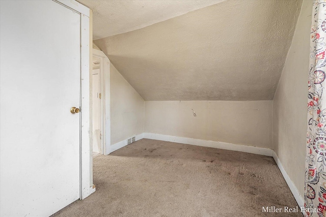 additional living space with carpet, visible vents, vaulted ceiling, a textured ceiling, and baseboards