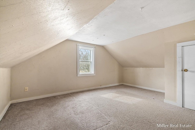 additional living space with a textured ceiling, carpet, lofted ceiling, and baseboards