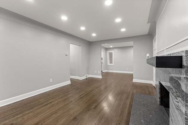 unfurnished living room featuring baseboards, dark wood-style flooring, a tiled fireplace, and recessed lighting