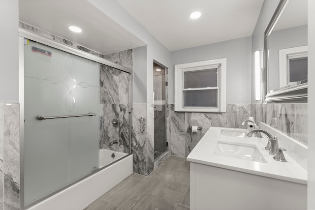 bathroom featuring double vanity, tile walls, bath / shower combo with glass door, and a sink