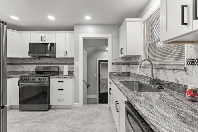 kitchen with stone counters, white cabinetry, stainless steel appliances, and a sink