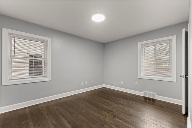 unfurnished room featuring dark wood-style flooring, visible vents, and baseboards