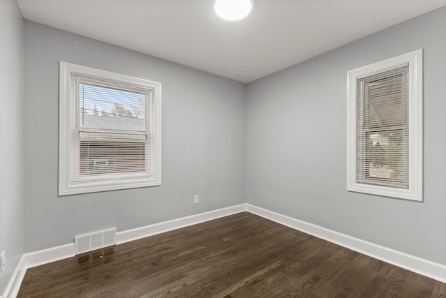 empty room featuring dark wood-style floors, visible vents, and baseboards