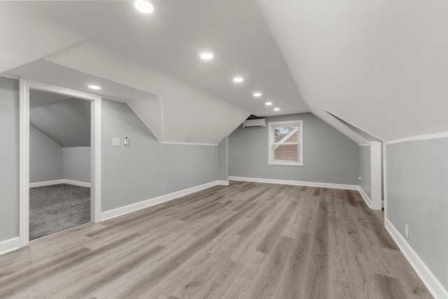 additional living space with lofted ceiling, light wood-style flooring, baseboards, and a wall mounted air conditioner