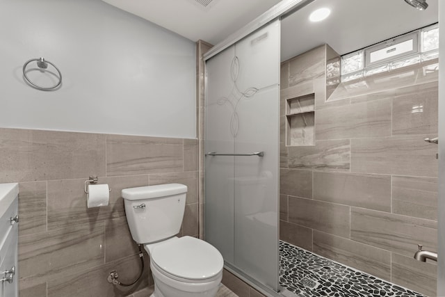 full bath featuring a wainscoted wall, a tile shower, toilet, and tile walls