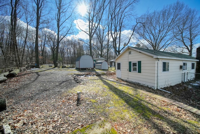 view of yard featuring dirt driveway, a shed, an outbuilding, and fence