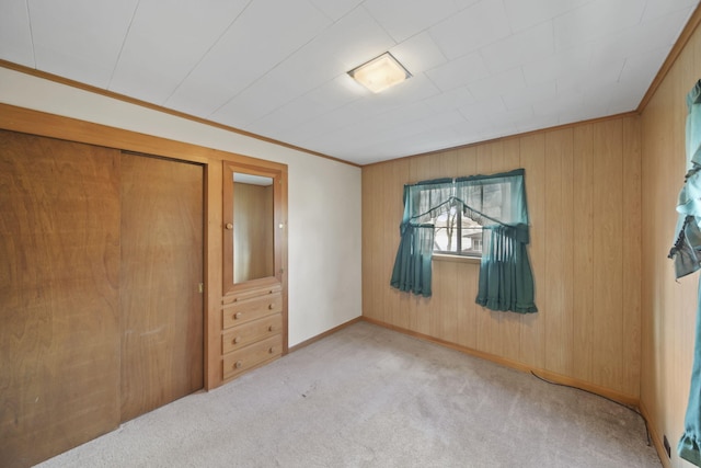 unfurnished bedroom featuring ornamental molding, carpet, wooden walls, and baseboards