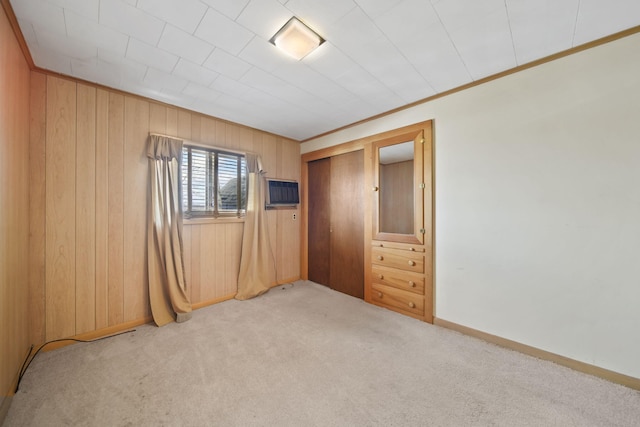 unfurnished bedroom with a wall unit AC, wood walls, ornamental molding, a closet, and carpet