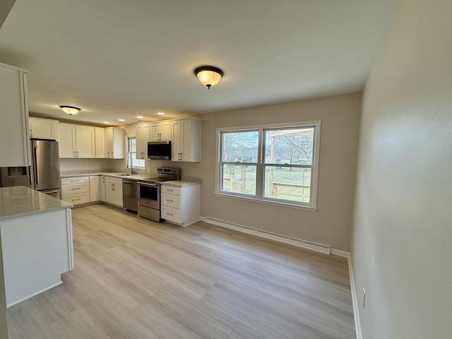 kitchen featuring stainless steel appliances, baseboard heating, a sink, and a wealth of natural light