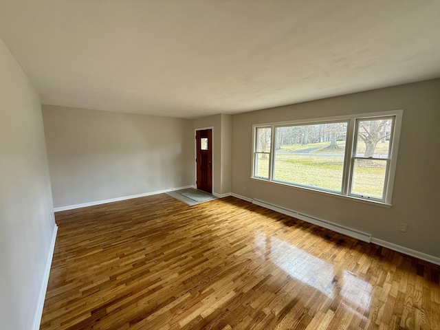 unfurnished room featuring a baseboard radiator, baseboards, and wood finished floors