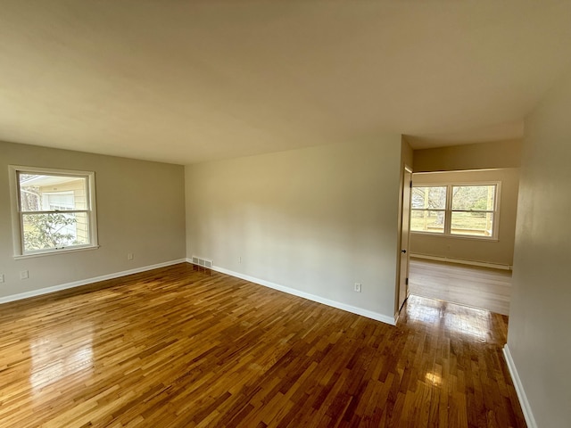 empty room featuring hardwood / wood-style floors, visible vents, and baseboards