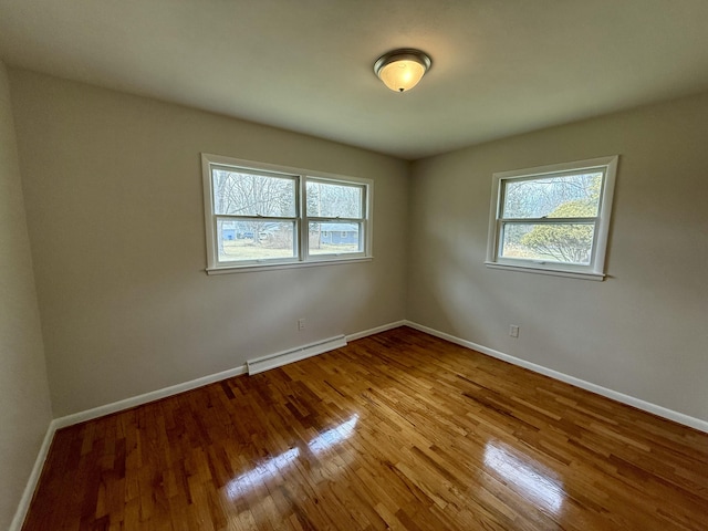 unfurnished room featuring baseboards, baseboard heating, and wood finished floors