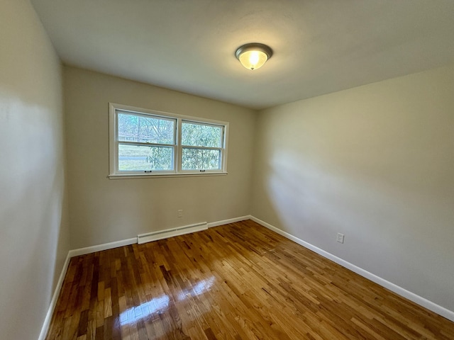 spare room with baseboards, a baseboard heating unit, and wood finished floors