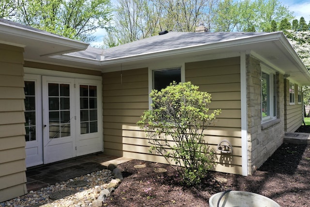 view of side of home featuring french doors, roof with shingles, and a chimney