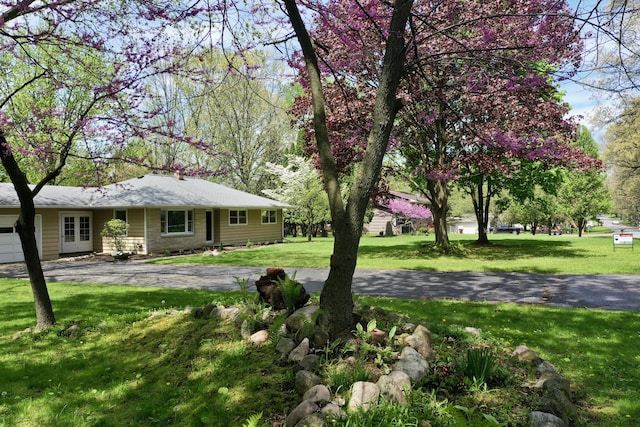 view of green lawn featuring a garage and asphalt driveway