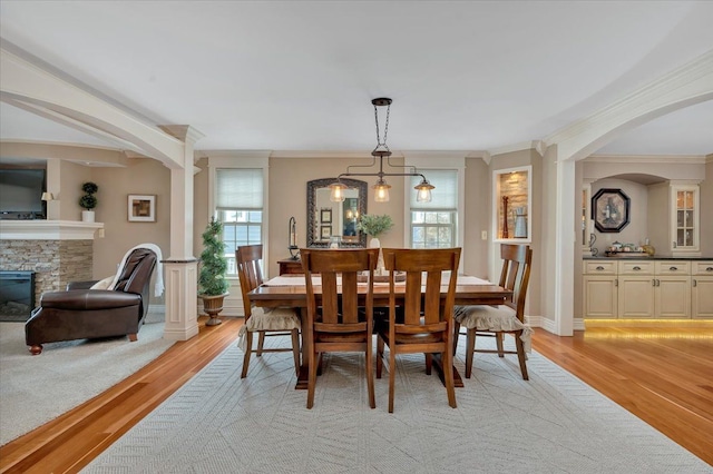 dining space with light wood-style floors, crown molding, a stone fireplace, and baseboards