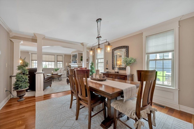 dining area featuring ornamental molding, light wood-style floors, baseboards, and ornate columns