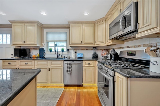 kitchen featuring cream cabinets, stainless steel appliances, a sink, light wood-type flooring, and tasteful backsplash