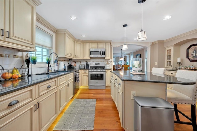 kitchen with light wood-style flooring, stainless steel appliances, a sink, cream cabinetry, and tasteful backsplash