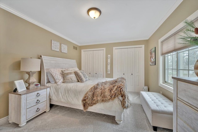 bedroom with crown molding, light carpet, visible vents, and multiple closets