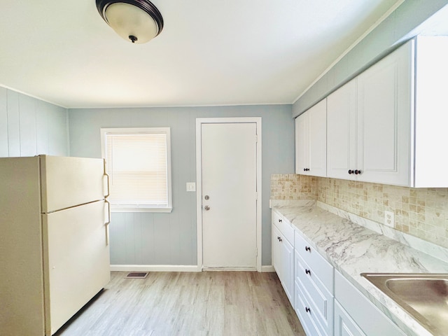 kitchen featuring tasteful backsplash, light wood-style floors, freestanding refrigerator, white cabinets, and a sink