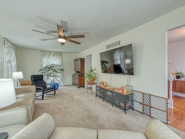 living room with carpet, visible vents, ceiling fan, and a textured ceiling