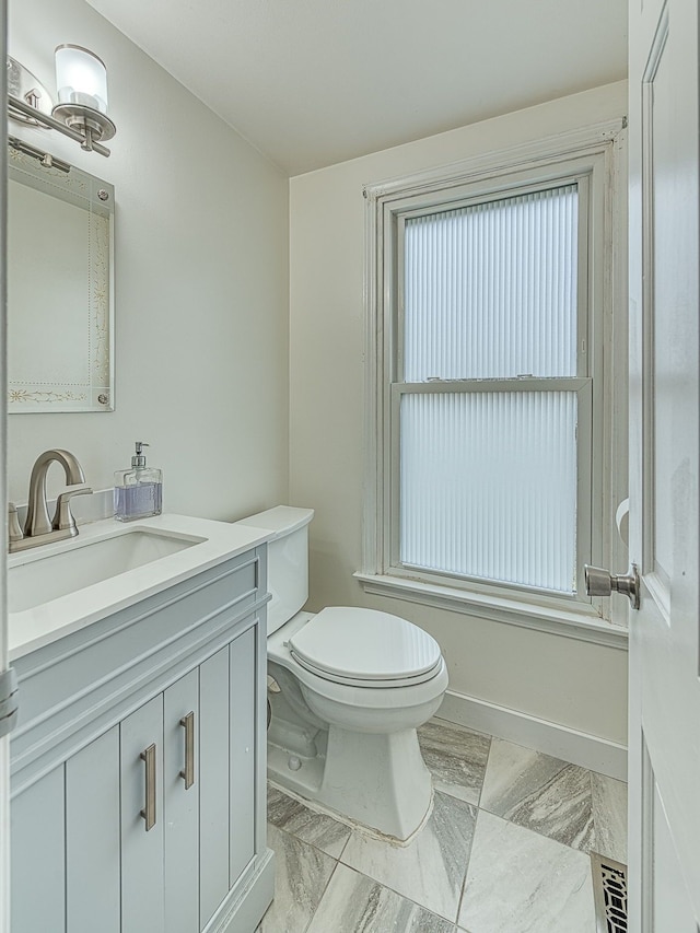 bathroom with marble finish floor, vanity, toilet, and baseboards