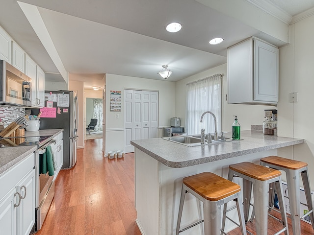 kitchen featuring white cabinets, a peninsula, stainless steel appliances, light wood-style floors, and a sink