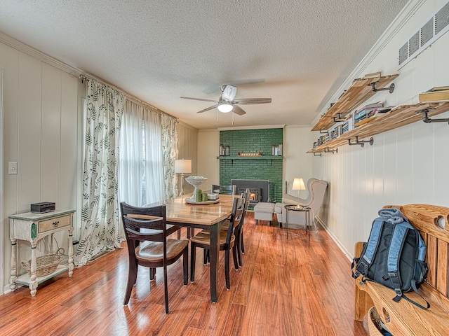 dining space with crown molding, a fireplace, visible vents, a ceiling fan, and wood finished floors